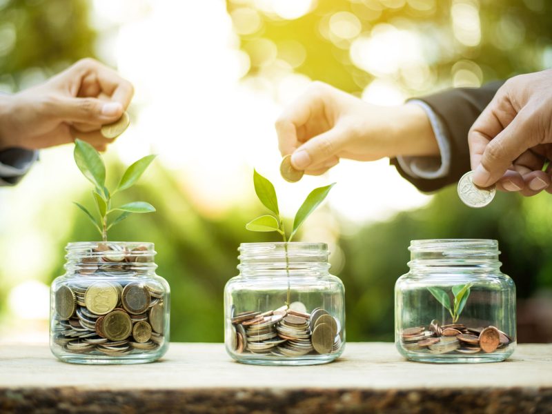 Businessman hands putting money (coin) into the glass jar - savings and investment  concept